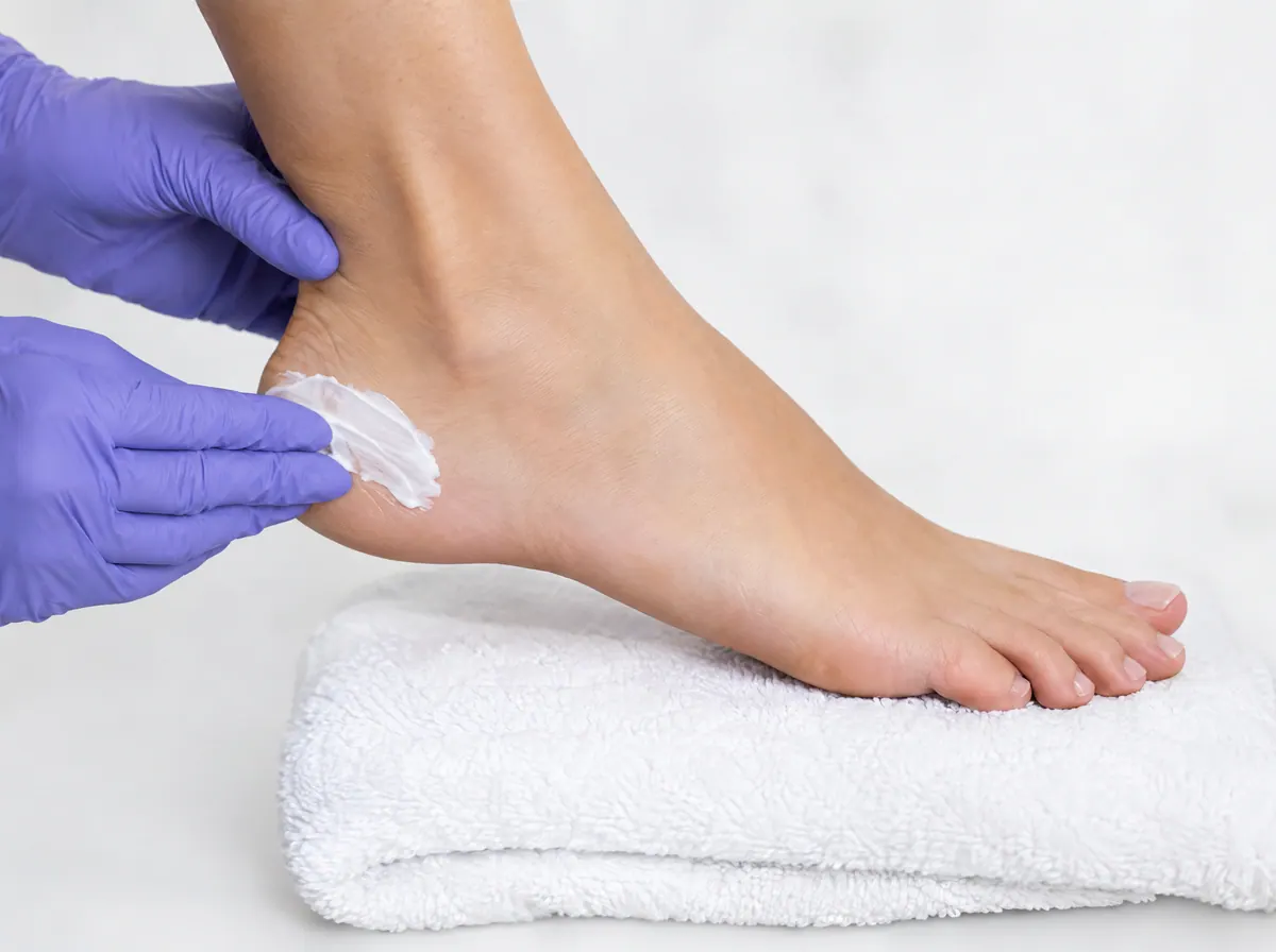 Hände in Handschuhen cremen einen Fuß auf einem weißen Handtuch ein